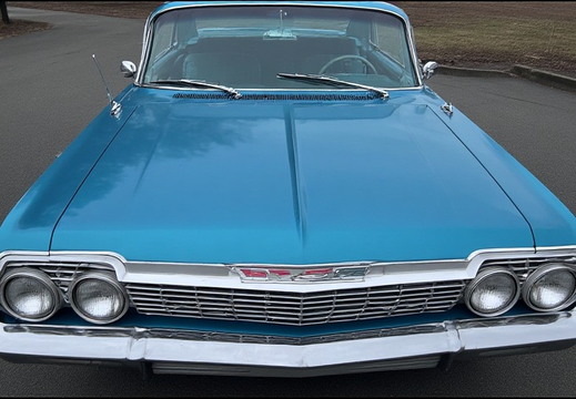 A front-facing view of a vintage, bright turquoise Chevrolet Impala.