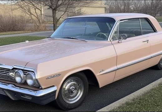This image showcases a vintage two-door Chevrolet Impala in a soft, pale pink color.