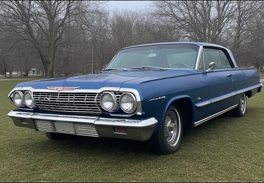 A classic blue Chevrolet Impala parked on a grassy area. 