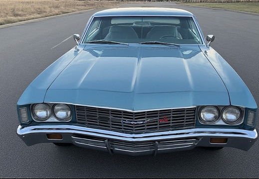 A head-on, slightly low-angle shot of a classic light blue Chevrolet Impala.